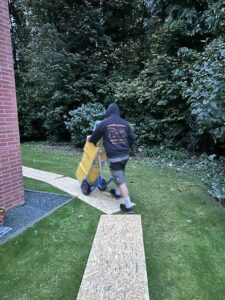 Déménageur utilisant un diable pour transporter une caisse lors d’un déménagement à Enghien, sur des planches pour protéger la pelouse